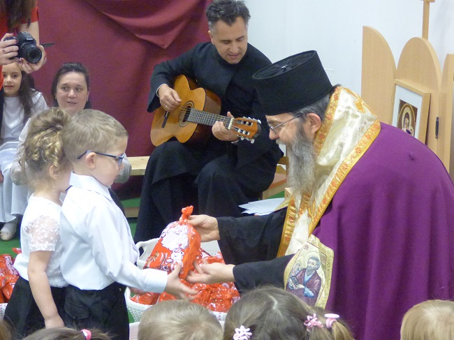 Atanáz püspök ajándékot ad át az óvodában, a háttrében Janka Gábor atya